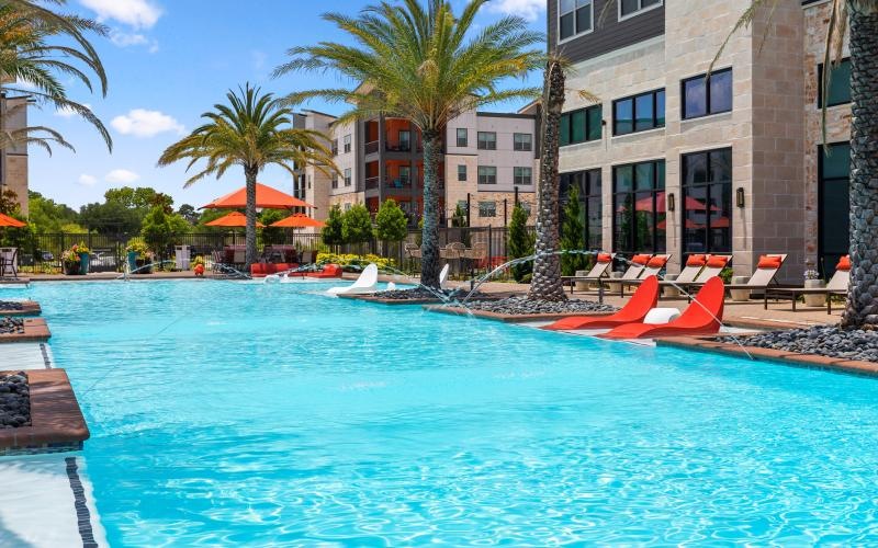 a pool with lounge chairs and umbrellas by a building